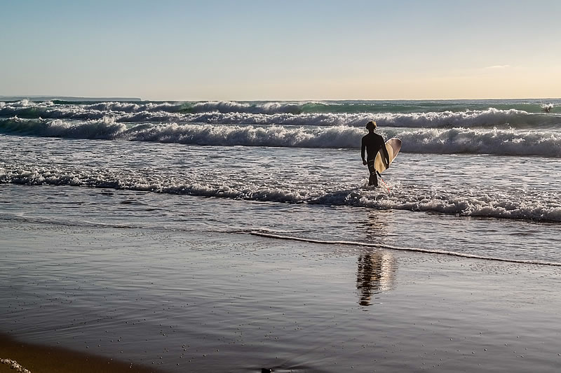 Surfer geht ins Wasser am Strand von Arrifana